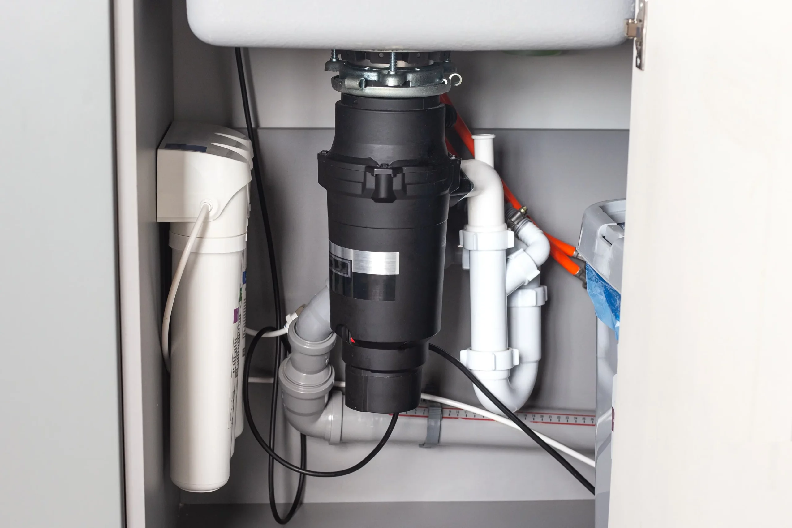 Professional garbage disposal installation under kitchen sink with gray disposal unit and proper plumbing connections