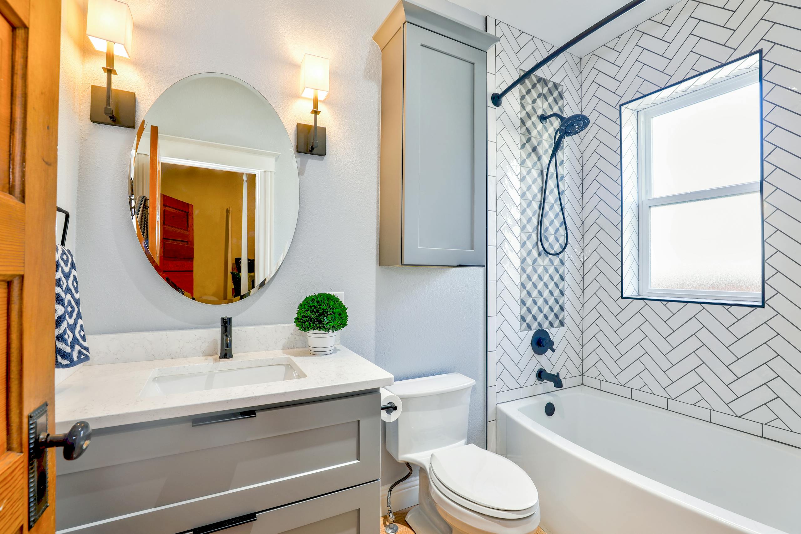 Elegant modern bathroom featuring chevron tiles, oval mirror, and sleek fixtures for a contemporary look. Also shown is a new plumbing installation with a toilet, shower, and sink